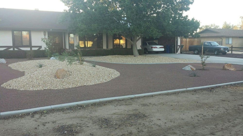 A house with a red gravel driveway and rock landscaping. A car is parked in the driveway and another in the garage.