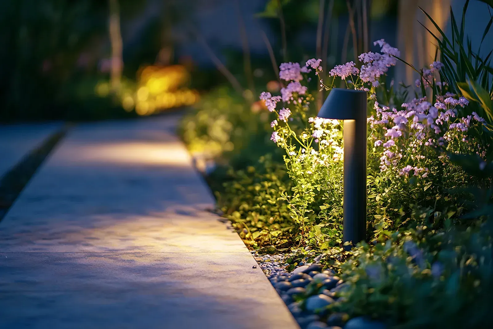 Outdoor landscape with path and trees lit by lights at night.