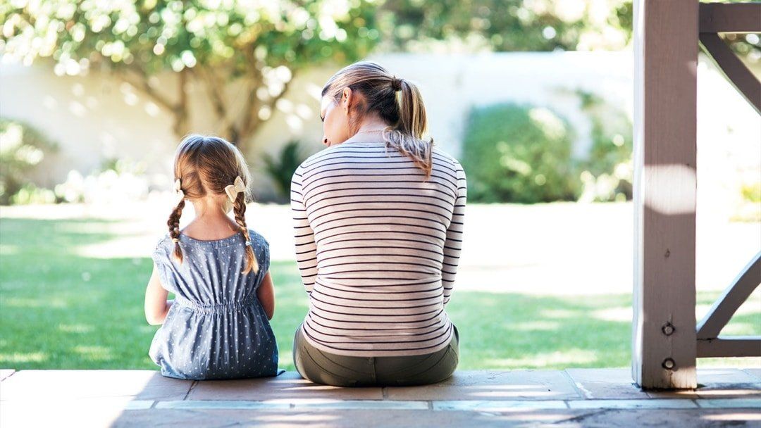 A woman and a little girl are sitting on a porch.