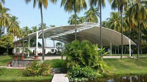 Una gran tienda blanca está rodeada de palmeras y un estanque.