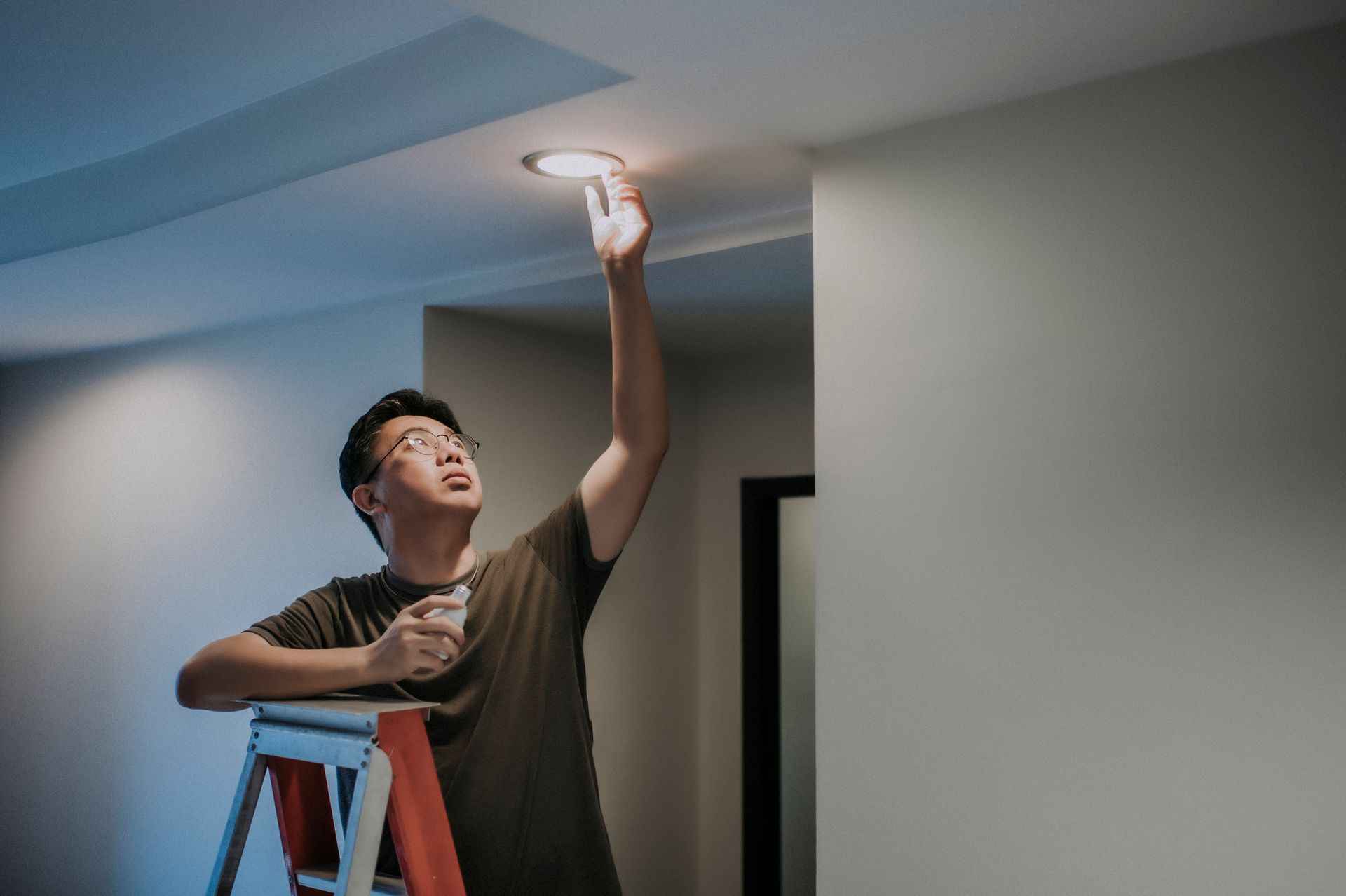 A man is standing on a ladder changing a light bulb — Las Vegas, NV — Discount Lighting Supply