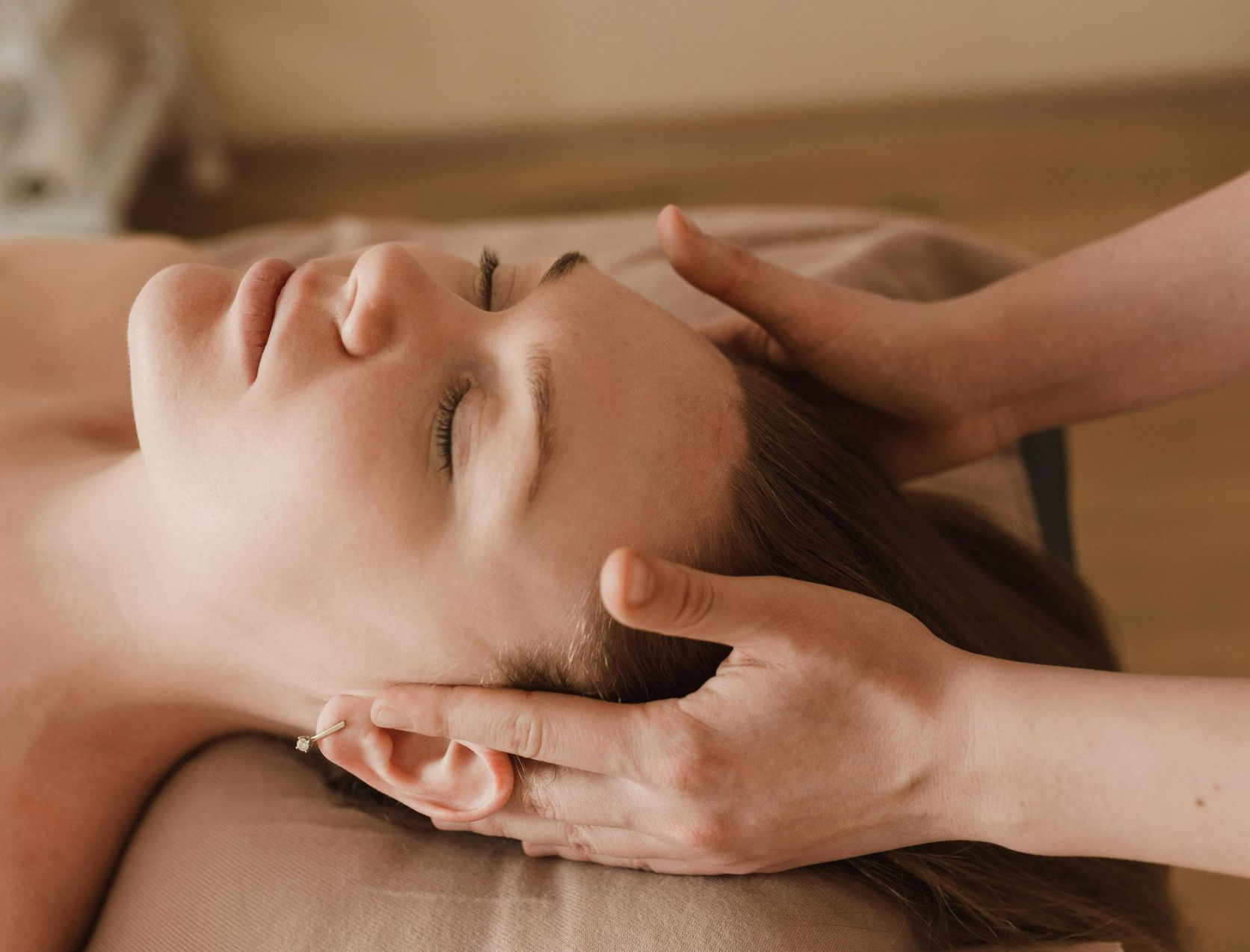 Woman receiving a head massage with closed eyes, hands on her head in a spa setting.