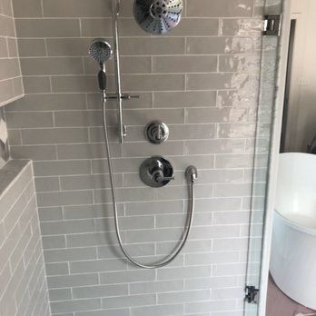 Gray tiled shower with chrome fixtures including a rainfall showerhead, handheld sprayer, and faucet controls.