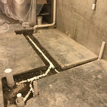 Concrete basement floor with trenches cut for white plumbing pipes; three vent pipes stand upright.