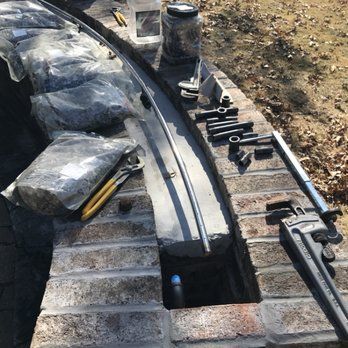 Brick structure under construction with tools laid out, including a pipe, sockets, and wrench, in an outdoor setting.