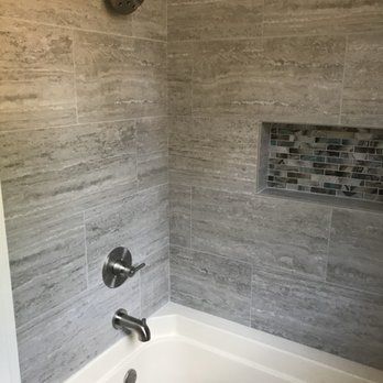 Gray tiled shower with a built-in shelf of mosaic tiles, chrome fixtures, and a white bathtub.