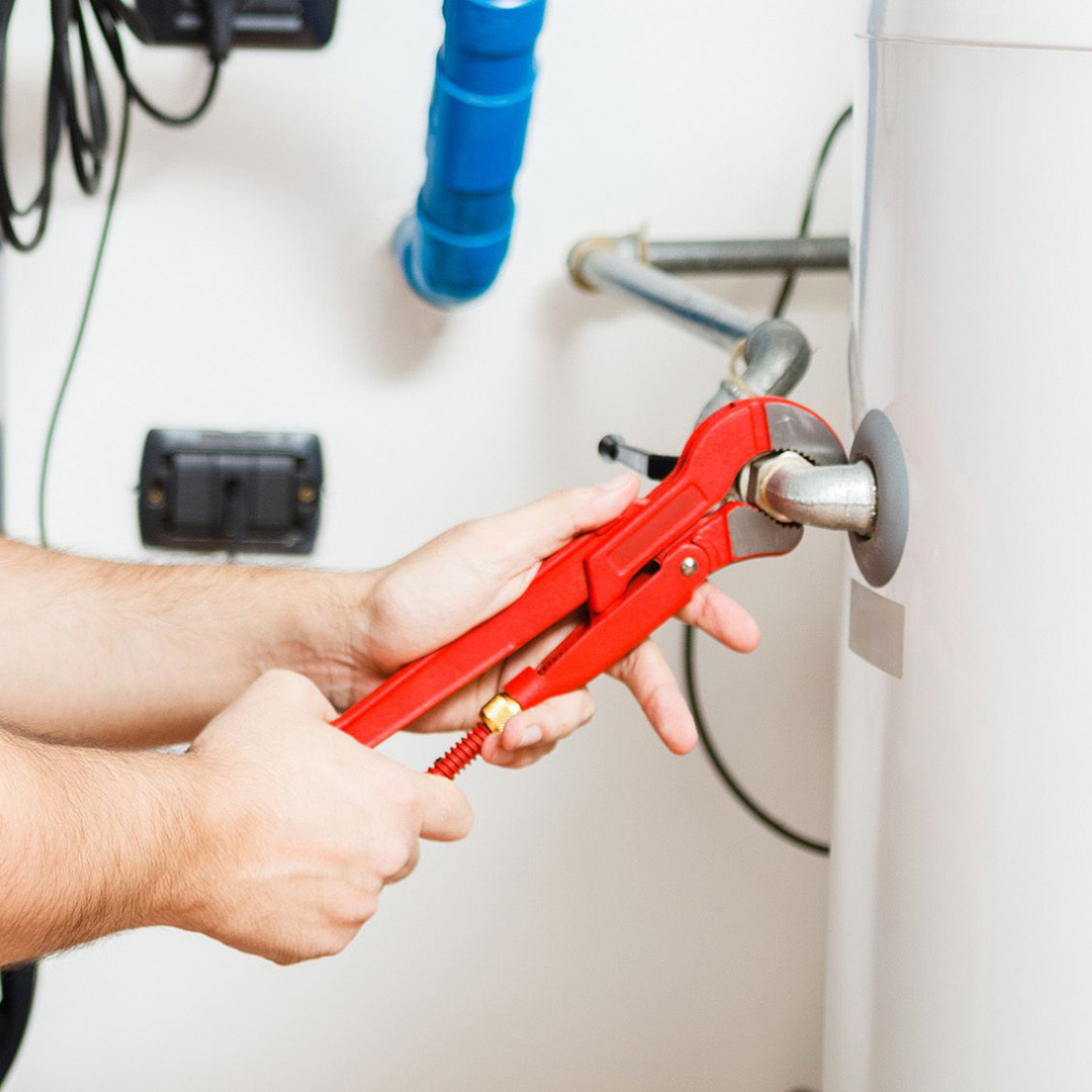 Person using red pipe wrench to work on a white water heater.