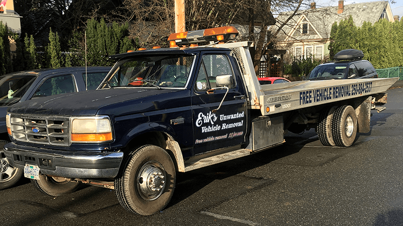 A tow truck with a flat bed is parked in a parking lot