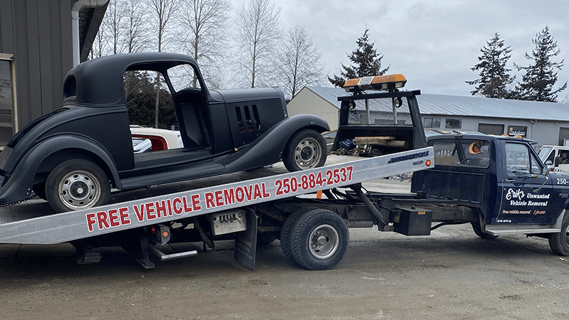 An old black car is being towed by a tow truck.
