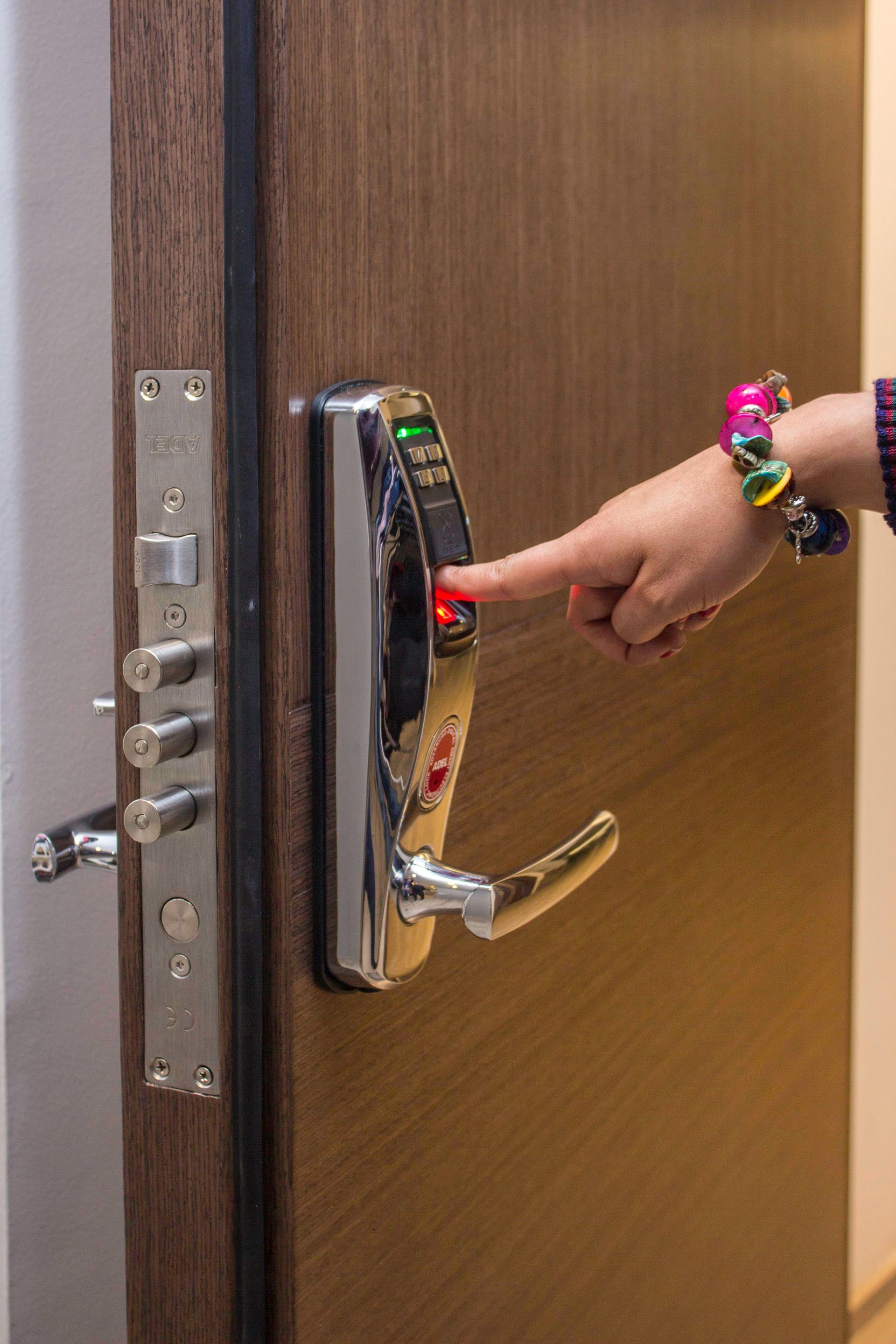 Hand pressing a red-lit door keypad on a wooden door with a metal lock and handle