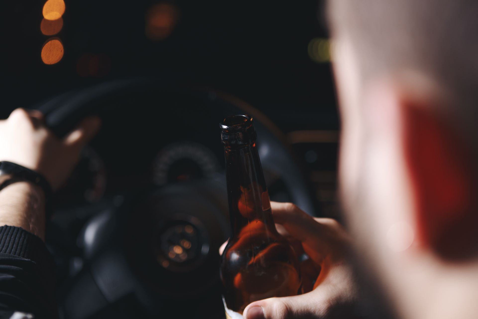 Person driving a car at night, holding a beer bottle.