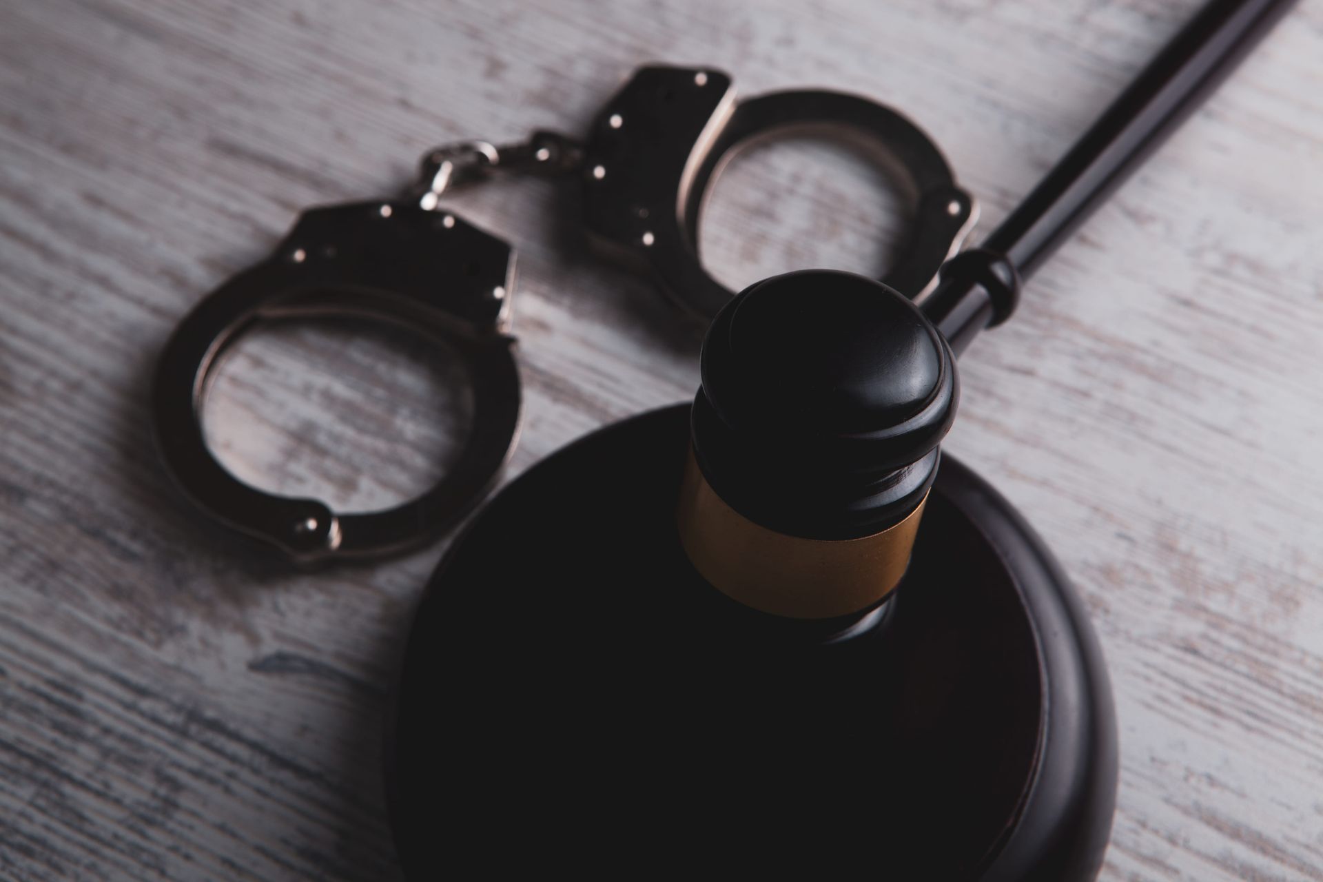 A judge's wooden gavel and a pair of metal handcuffs resting on a light-colored, textured wooden surface.