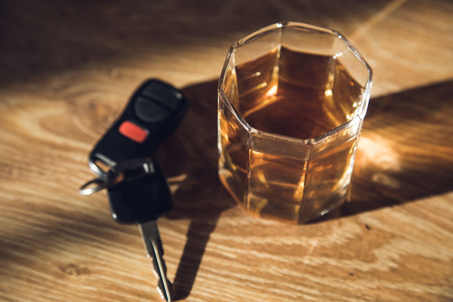 A glass of whiskey and a car key on a wooden table.