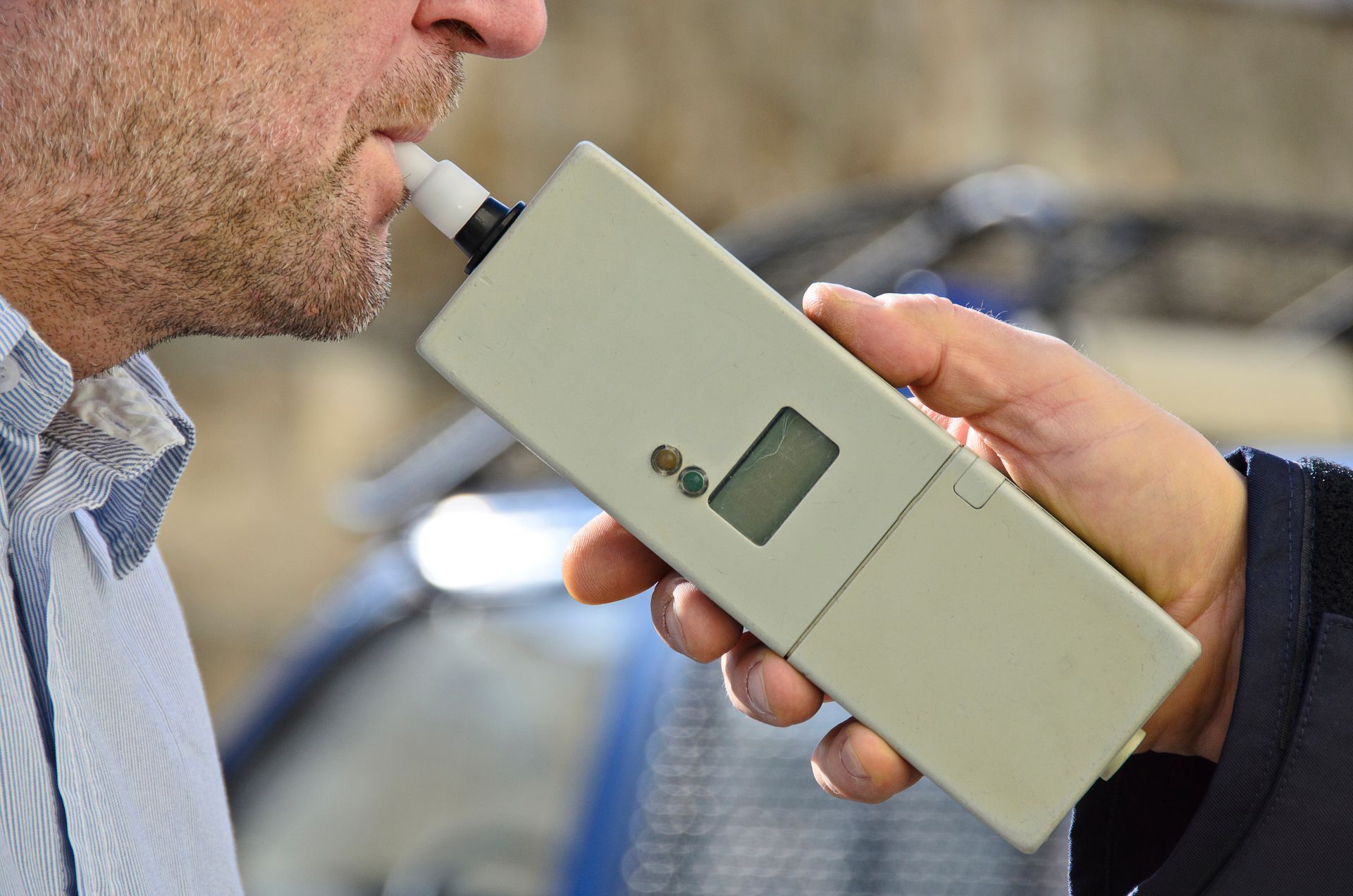 Man blowing into a breathalyzer held by another person, presumably during a roadside sobriety test.