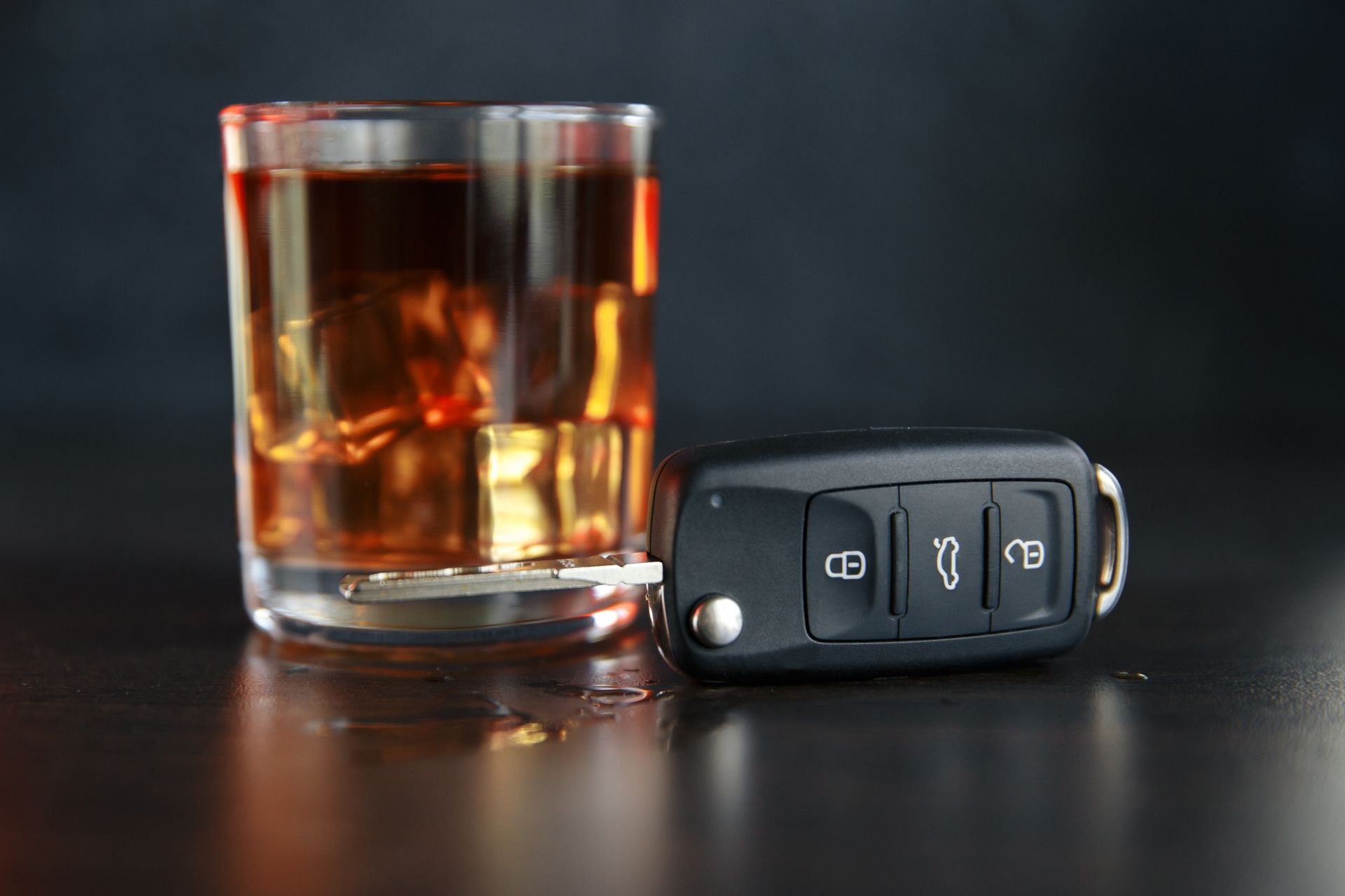 A glass of whiskey and a car key on a table.