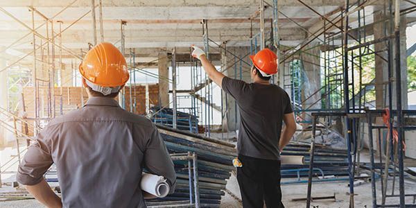Deux personnes portant des casques de chantier sur un chantier. L'une pointe vers le haut tandis que l'autre tient un plan enroulé.