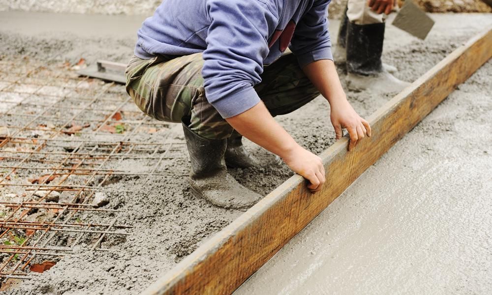 Personne nivelant du béton humide avec une longue planche de bois.
