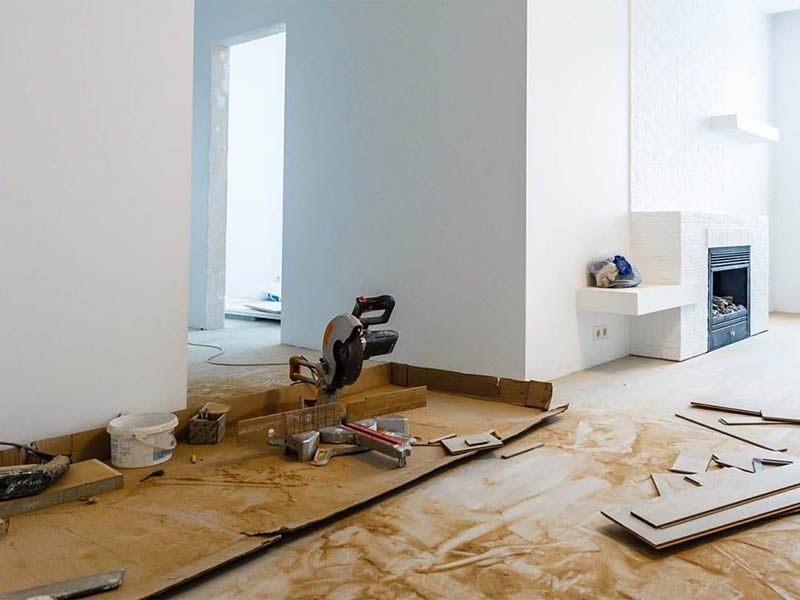 Intérieur en cours de rénovation avec scie à onglet, outils et revêtements de sol. Murs blancs, cheminée.