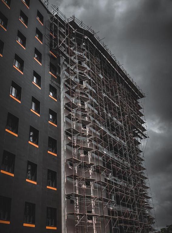 Grand bâtiment sombre en construction ; un échafaudage en recouvre un côté. Ciel couvert.