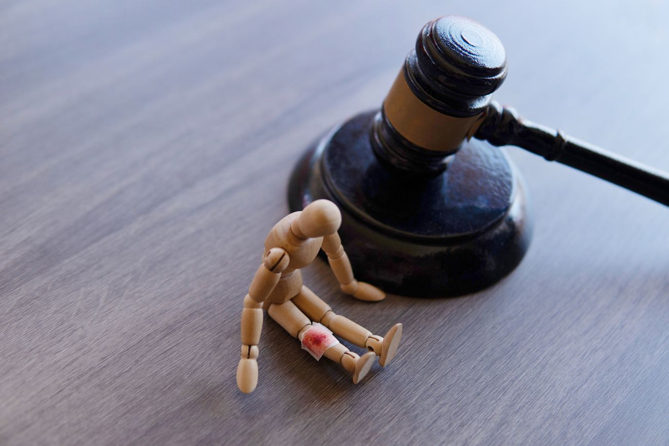 Wooden mannequin with a red mark on its knee sitting next to a gavel.