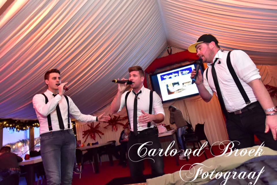 Drie mannen zingen in microfoons in een tent.