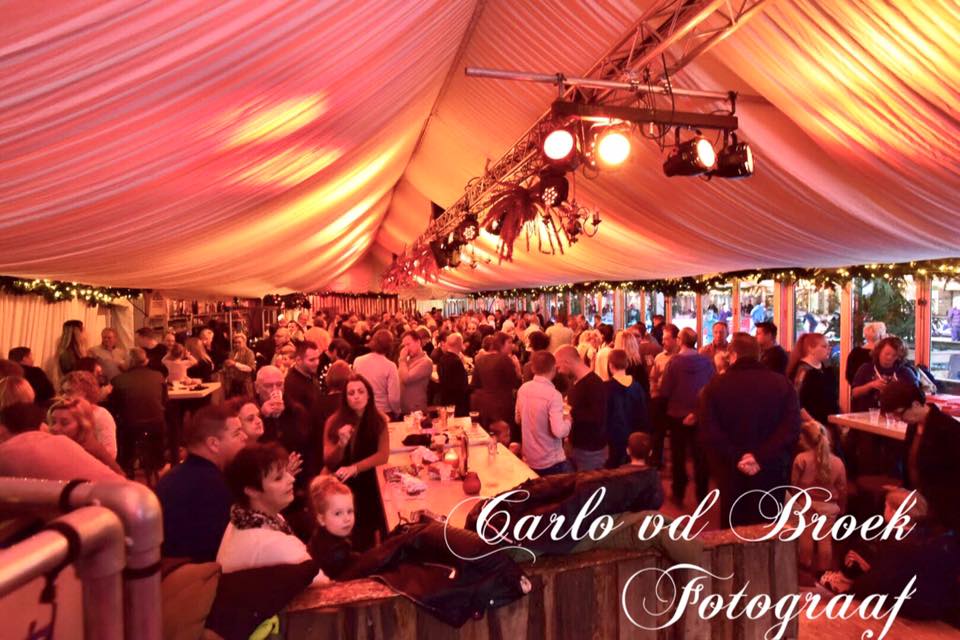 Een grote groep mensen is verzameld onder een tent gesponsord door carlo vd broek
