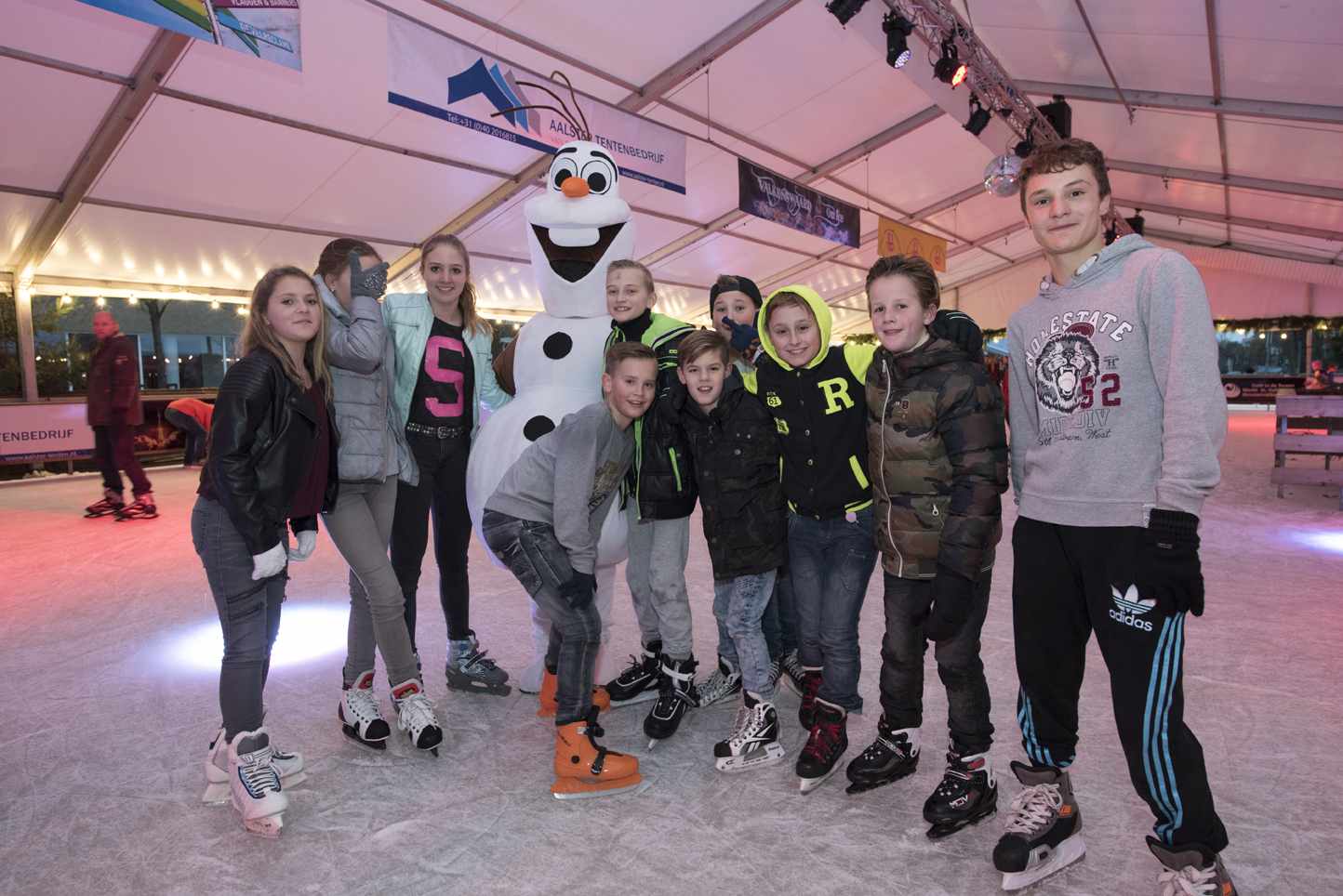 Een groep kinderen poseert voor een foto met een sneeuwpop op een ijsbaan.