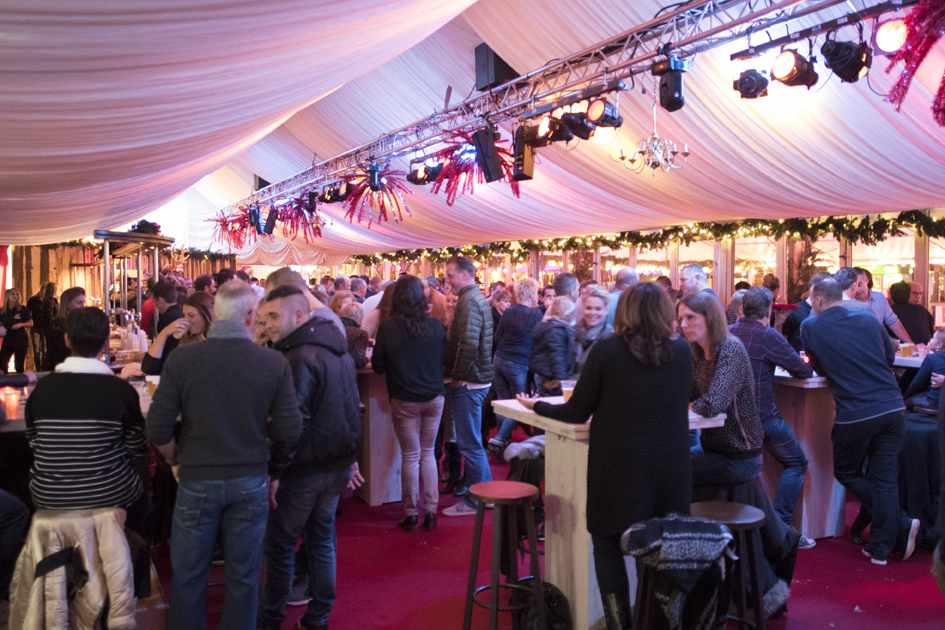 Een grote groep mensen zit aan tafels in een tent.