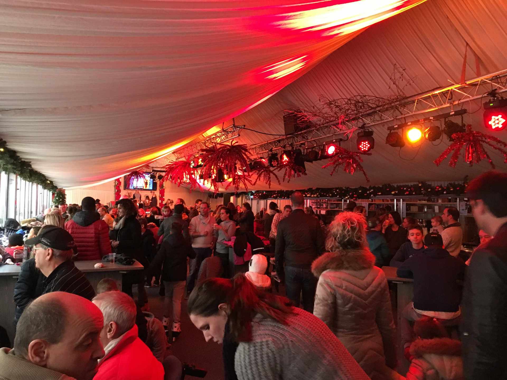 Een grote groep mensen is verzameld in een grote ruimte met rode lichten aan het plafond.