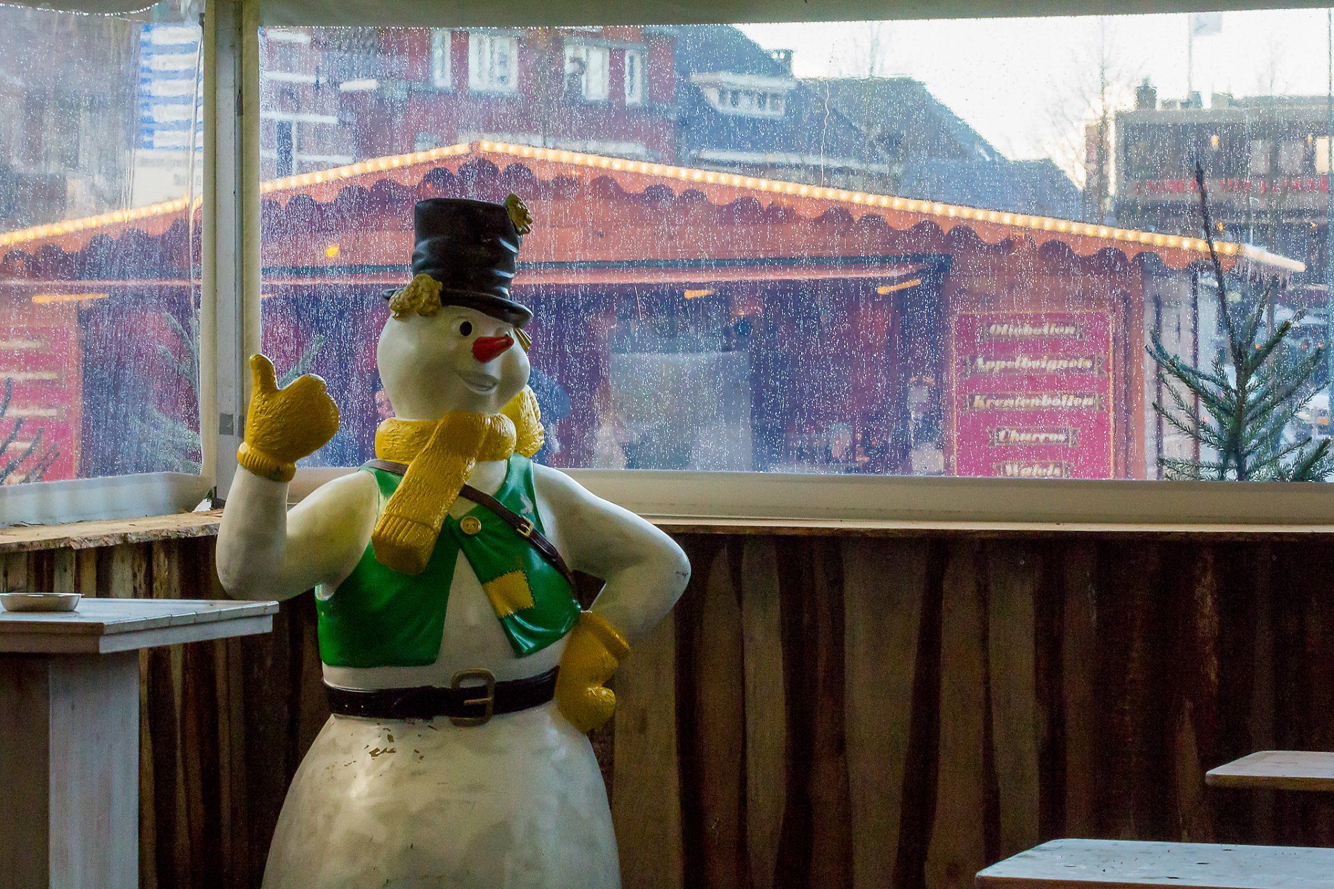 Een sneeuwmanbeeld steekt zijn duim omhoog voor een raam.