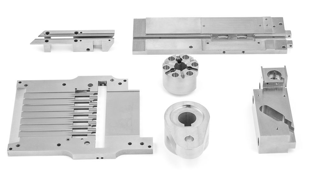 Een aantal metalen onderdelen liggen op elkaar op een wit oppervlak.