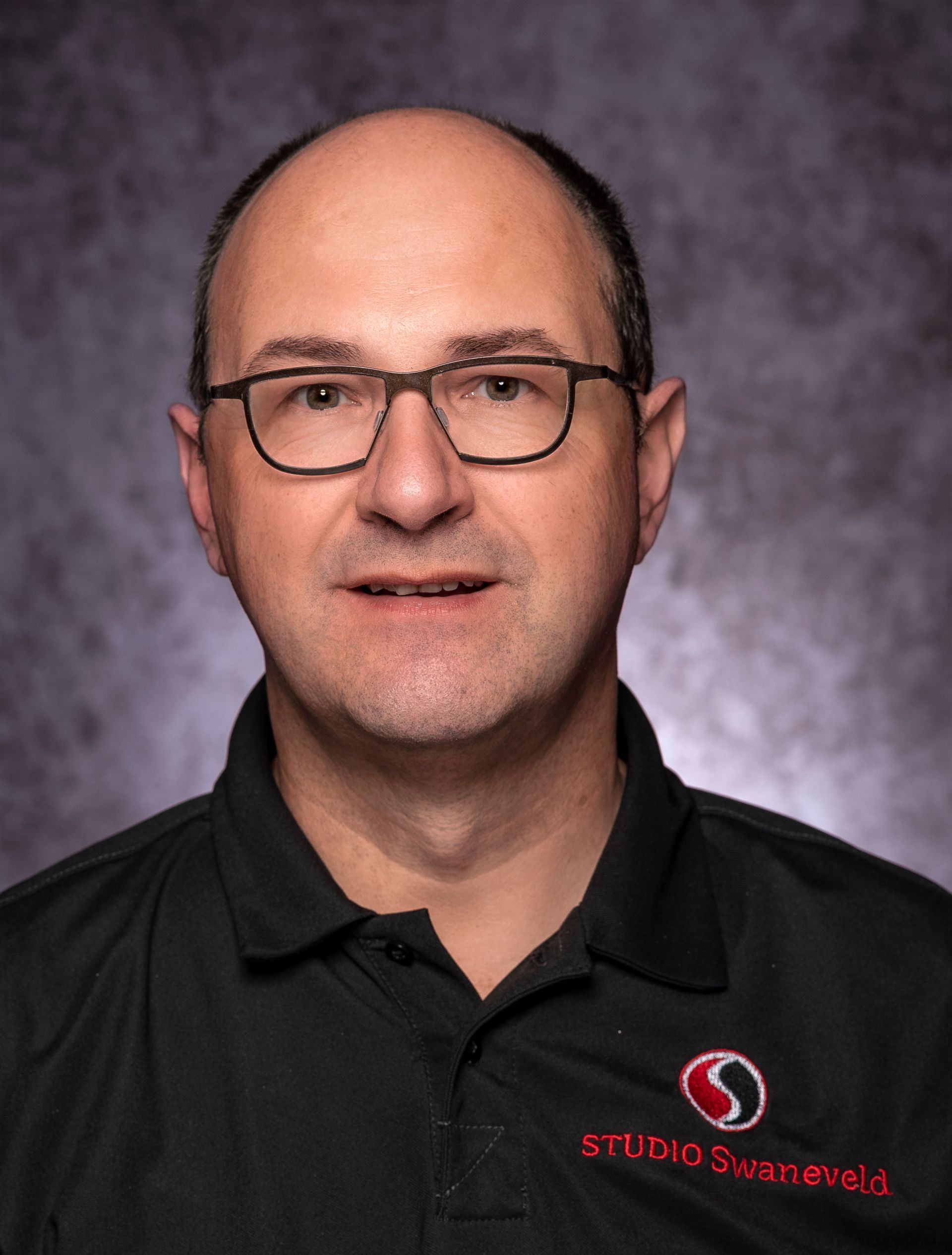  fotograaf met bril en een zwart poloshirt met het bedrijfslogo.