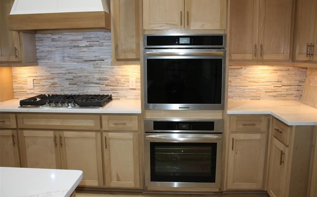 Kitchen with light wood cabinets, stainless steel double oven, gas cooktop, and white countertops.