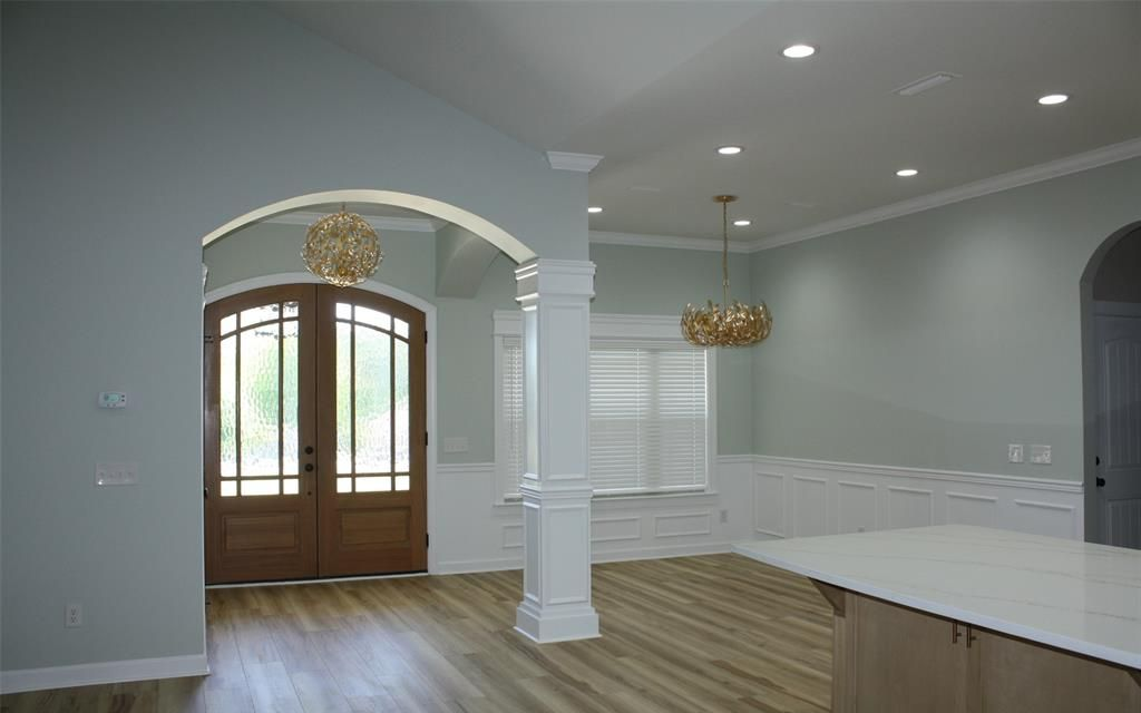 Interior of a house with light blue walls, arched doorways, wood floors, and chandeliers.