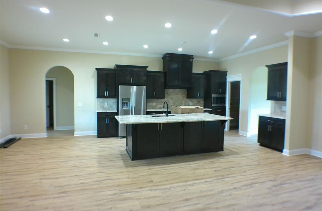 Spacious kitchen with dark cabinets, island, stainless steel appliances, light-colored floors, and beige walls.