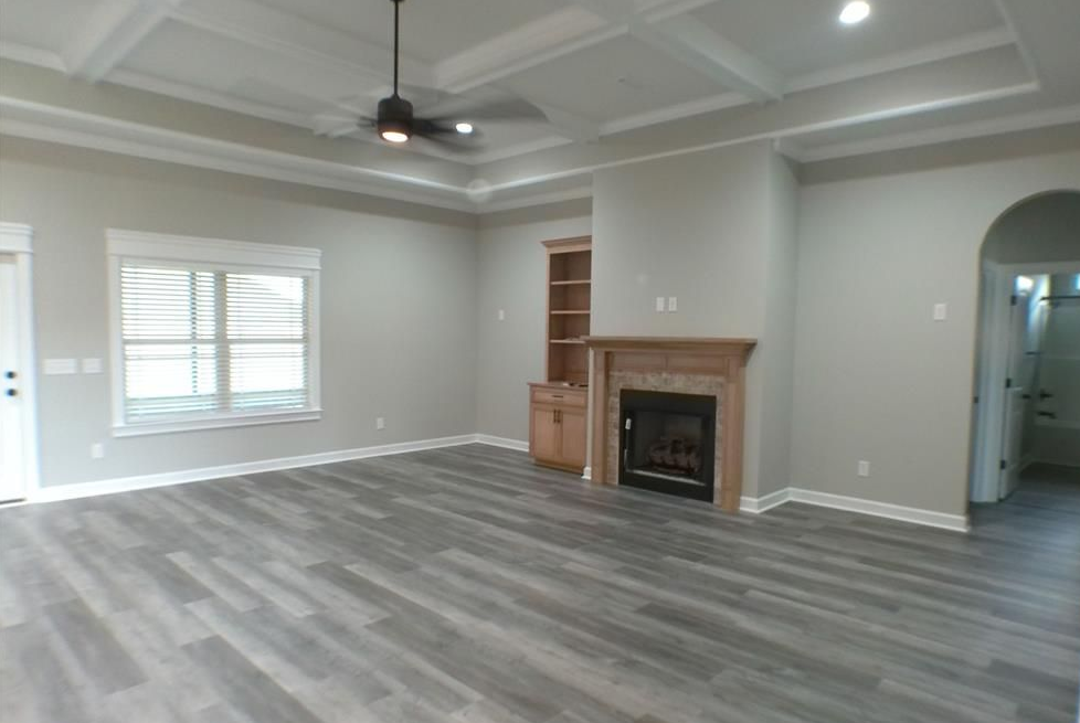Empty living room with grey flooring, fireplace, built-in shelves, and an arched doorway.