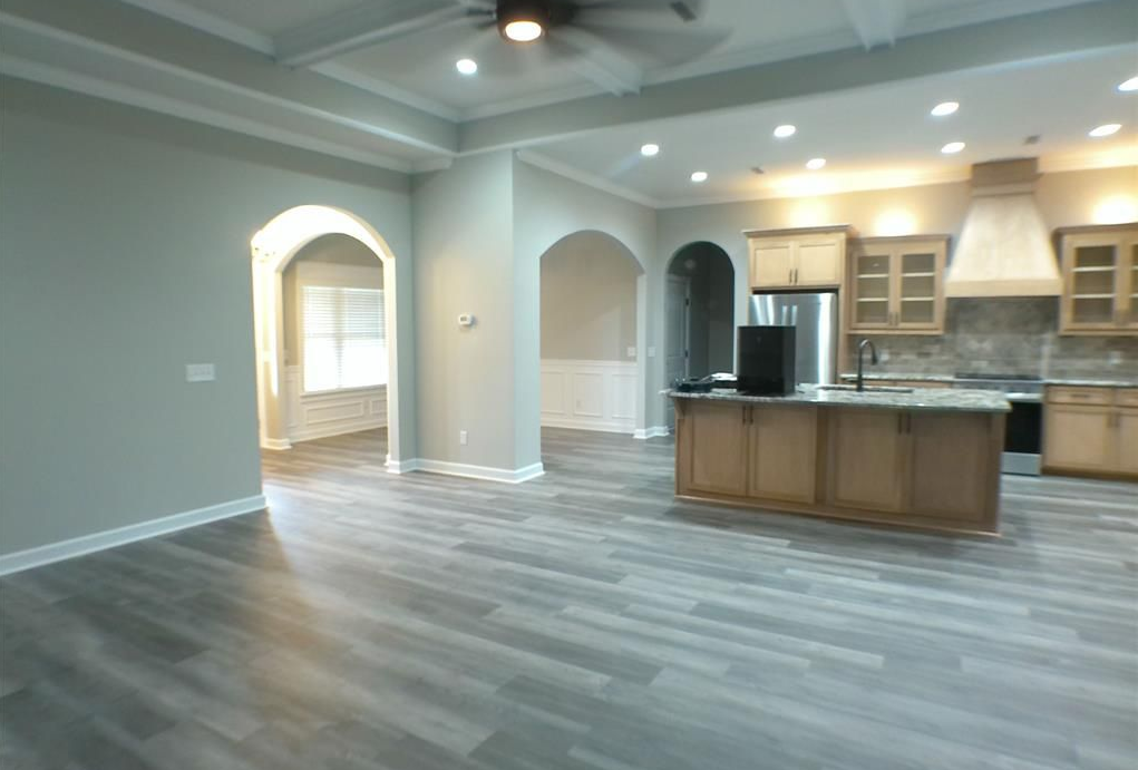 Open-concept kitchen and living area with gray wood-look floors, light cabinets, and arched doorways.