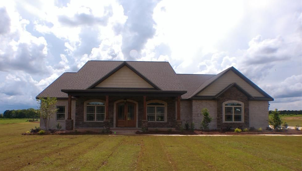Ranch-style house with brick and stone facade, front porch, and brown roof under a cloudy sky.