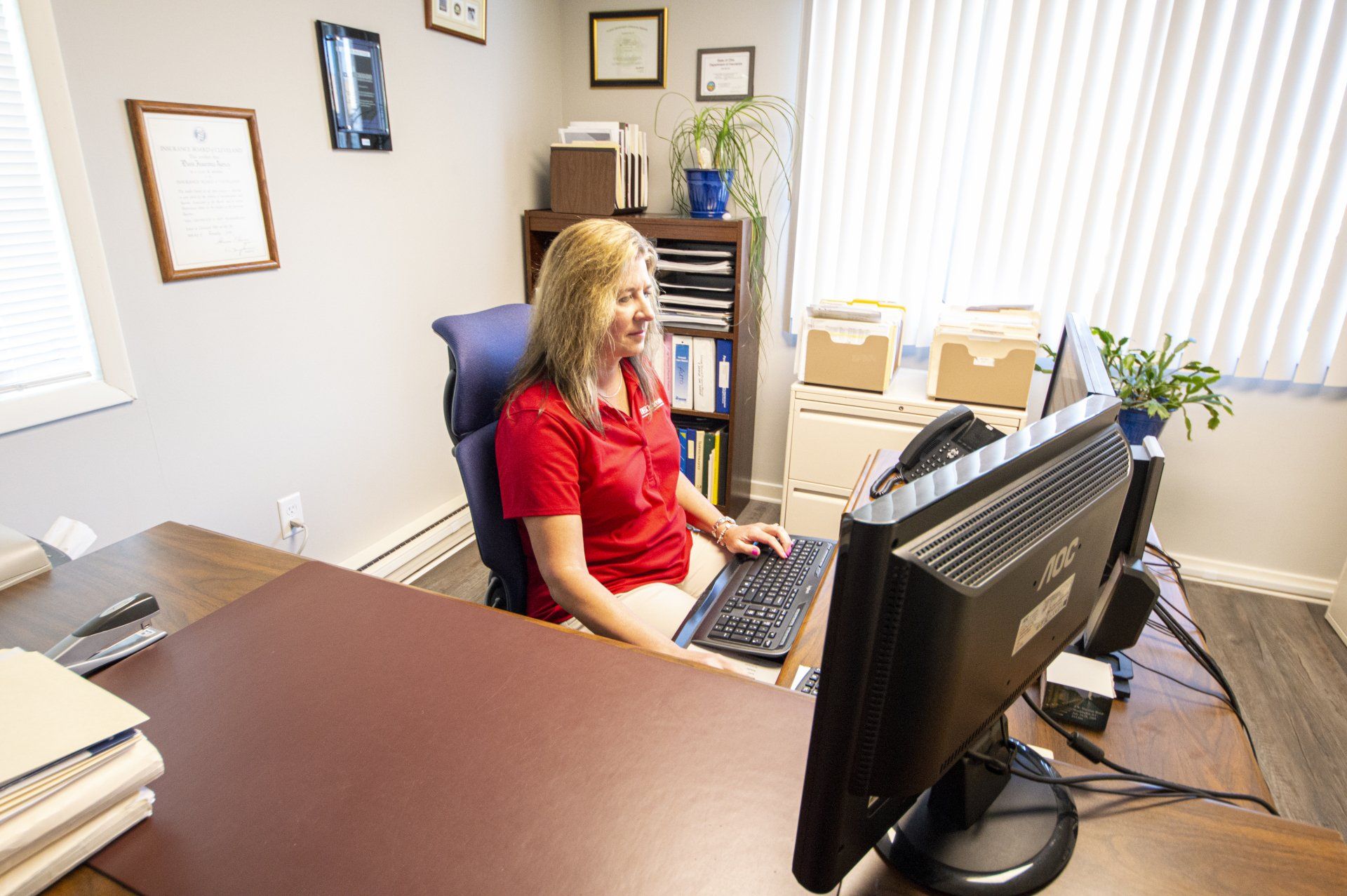 Woman in red shirt smiling at computer in office.