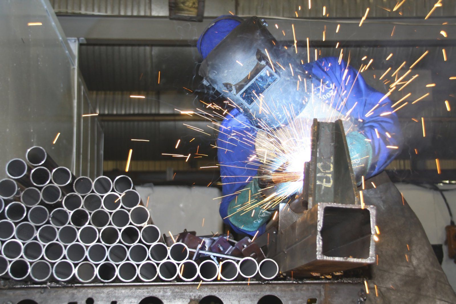 A welder in protective gear uses an arc welder on a metal frame, producing bright sparks in an industrial workshop.