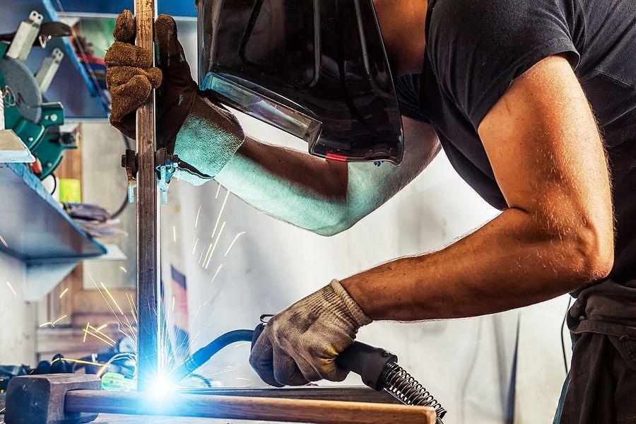 A welder in protective gear uses a welding torch to join metal pieces, creating bright sparks in a workshop.
