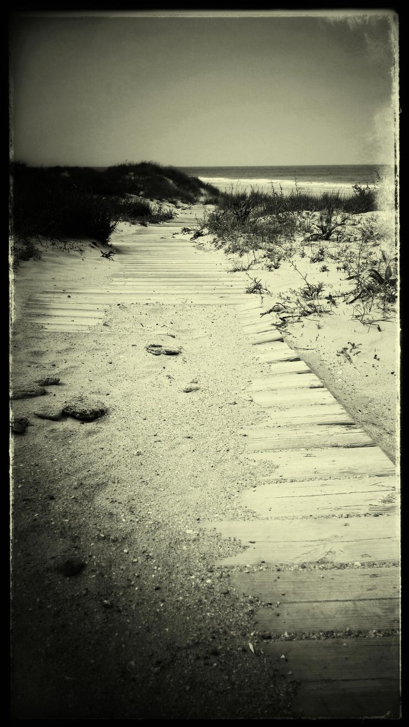 A black and white photo of a wooden walkway leading to the ocean
