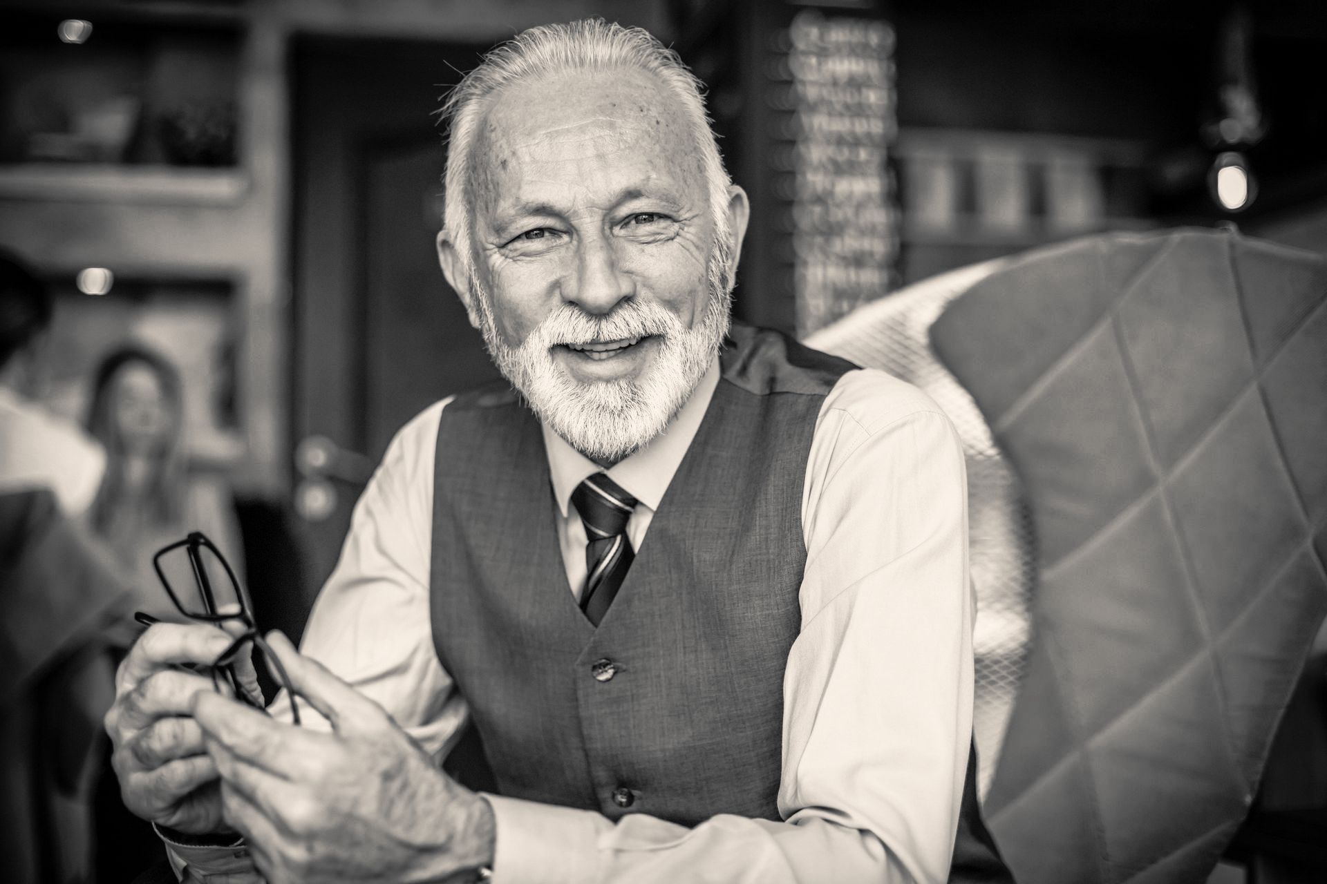 A black and white photo of an older man holding glasses.