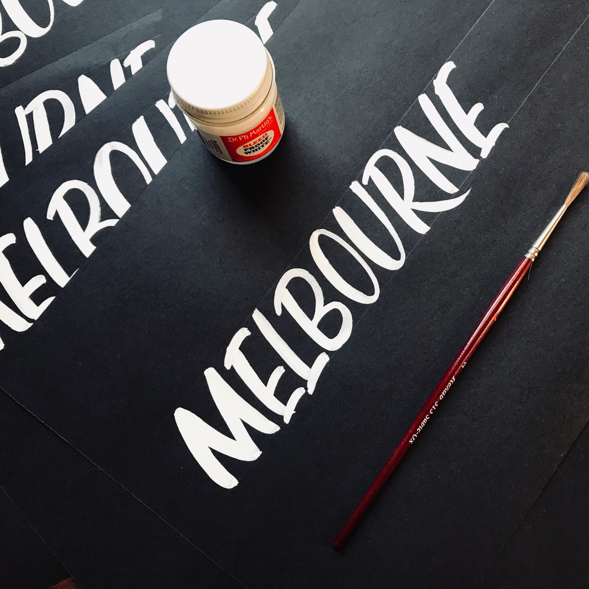 'Melbourne' brush calligraphy using Dr Martin's Bleedproof white on a black texture cardboard.