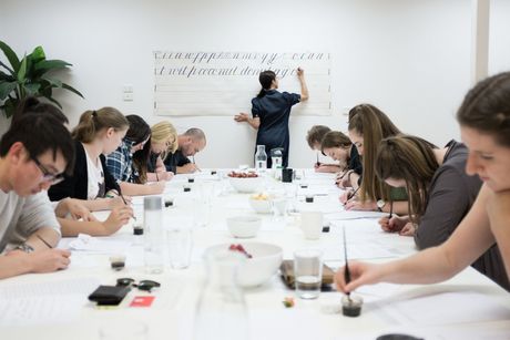 Portrait image of Maria Montes and a student of her at a desk reviewing some calligraphy writing.
