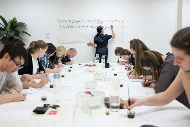 Portrait image of Maria Montes and a student of her at a desk reviewing some calligraphy writing.