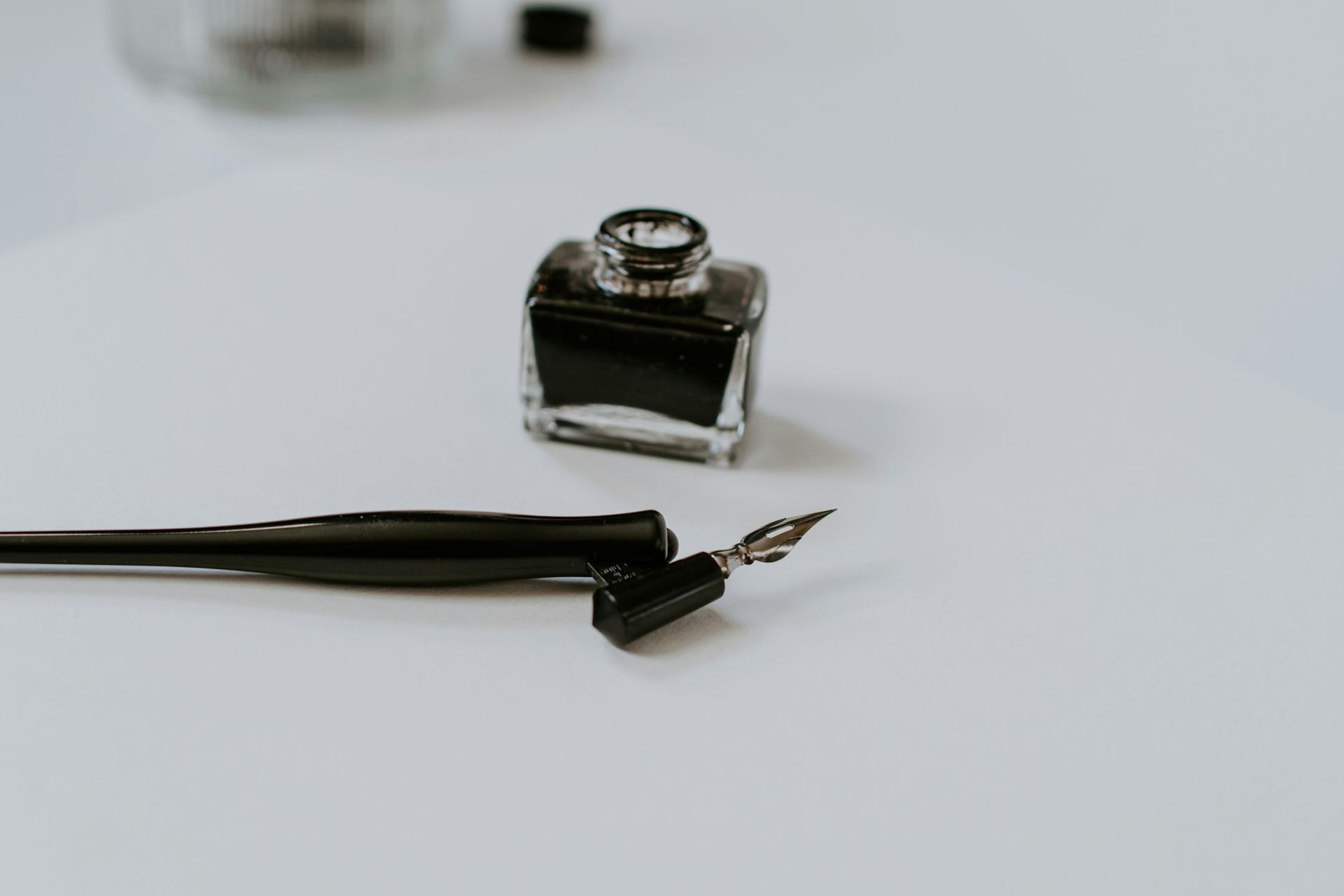 An oblique calligraphy pen holder and a black ink bottle on a white table.