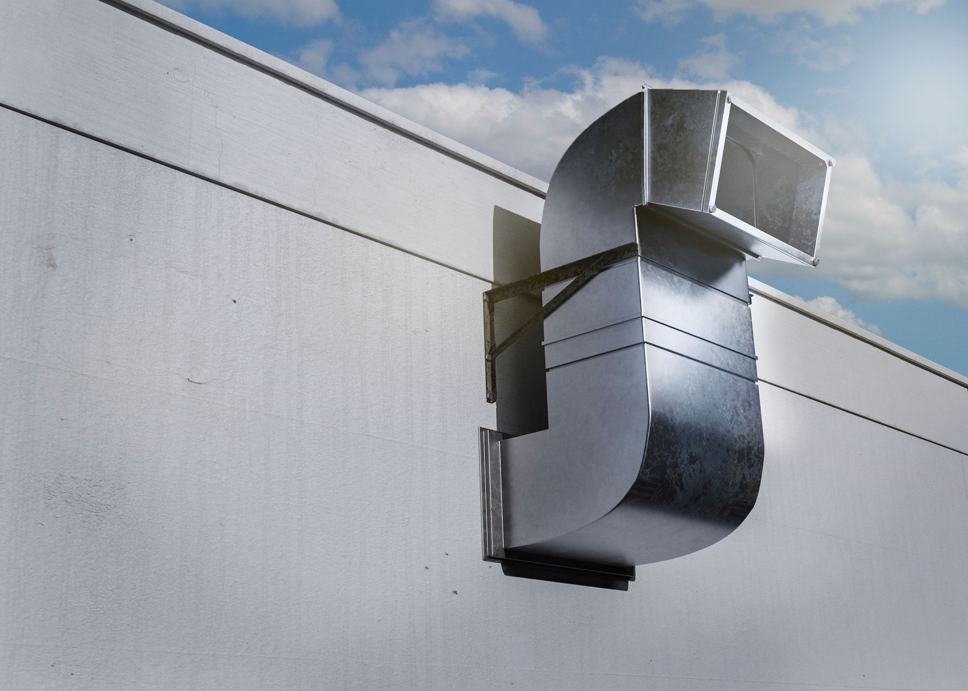 Metallic air duct curving out of a white wall against a partly cloudy blue sky.