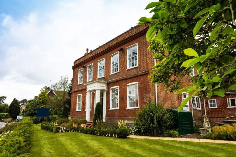 Red brick Georgian house with white columns, windows, and green lawn.