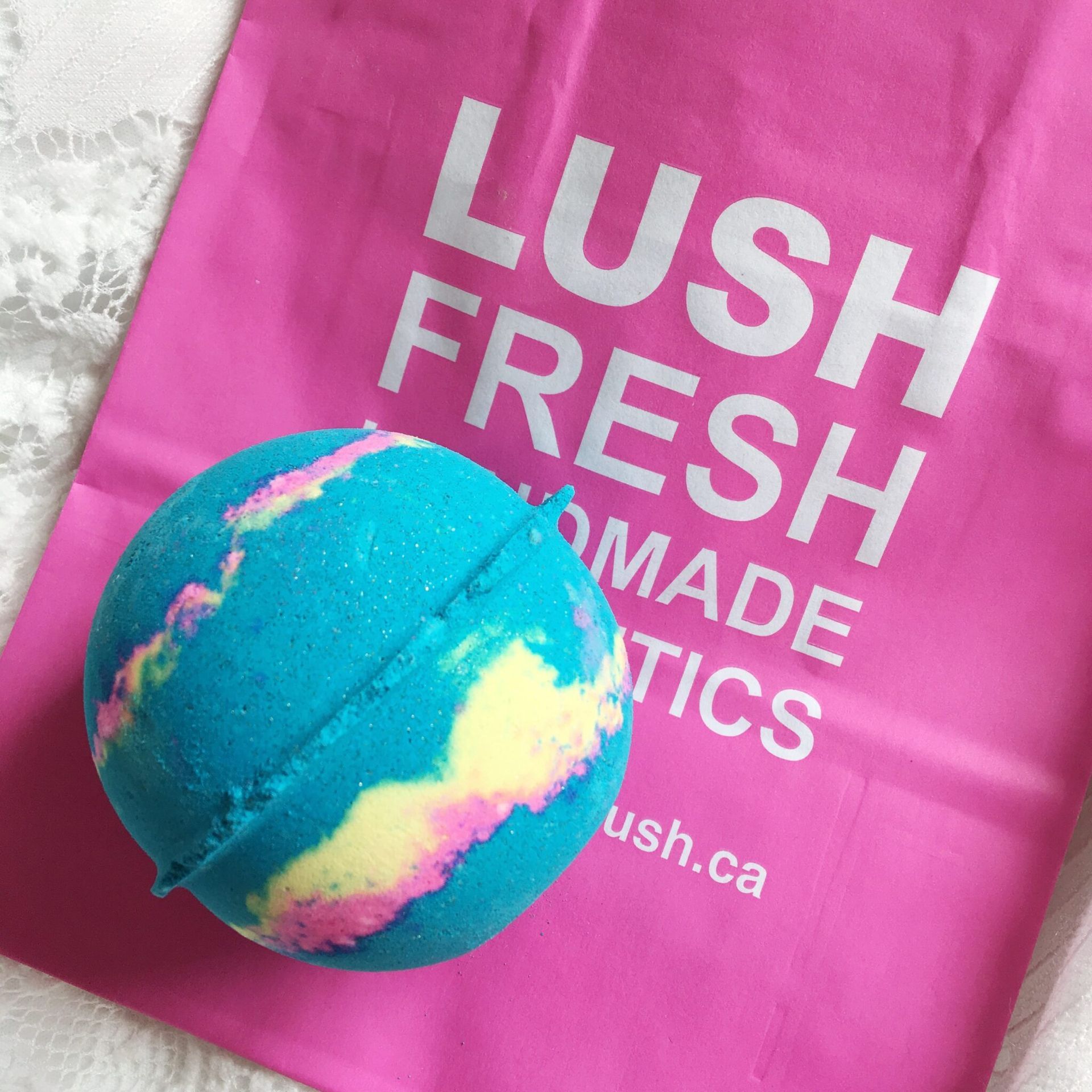 Blue and multicolored bath bomb next to a pink Lush shopping bag.